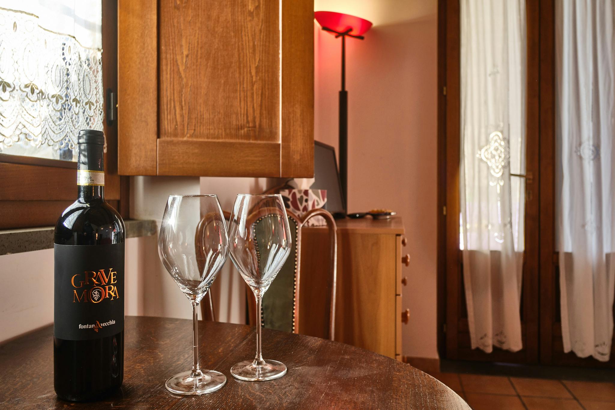 Dettaglio di due calici e una bottiglia di vino Grave Mora delle cantine Fontana Vecchia sul tavolino dello Chalet della tenuta Le Pietre a Pietrelcina